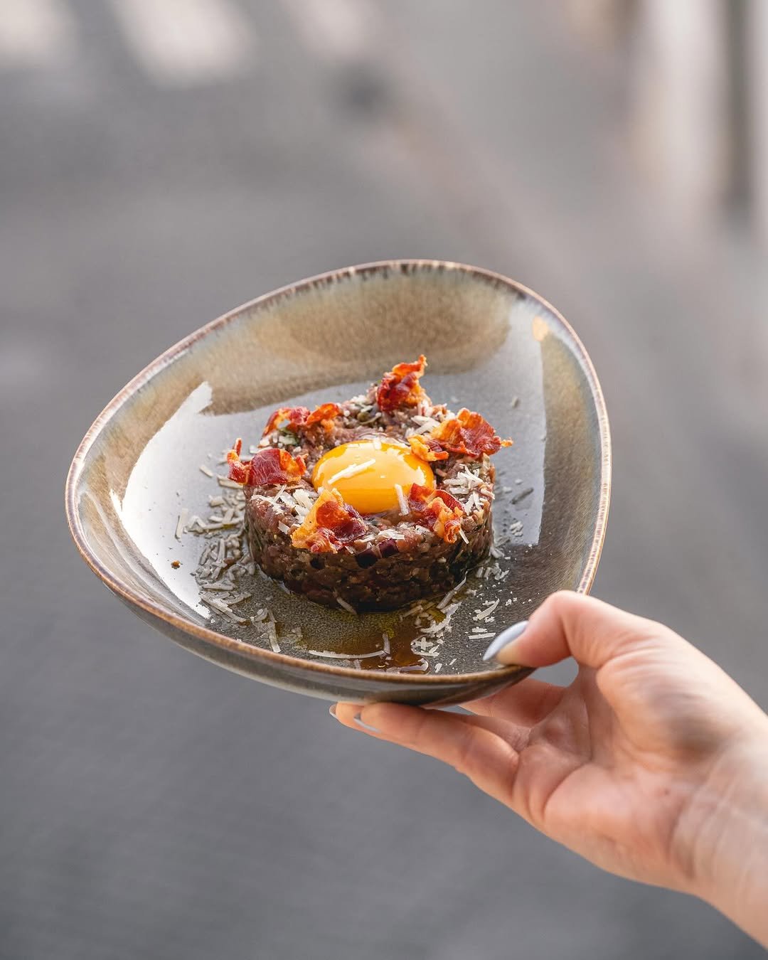 Tártaro de novilho com gema de ovo, lascas de bacon e parmesão num prato oval
